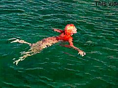 A girl relaxes in blue water while naked outdoors.